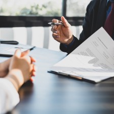Businessman in suit in his office showing an insurance policy and pointing with a pen where the policyholder must to sign. Insurance agent presentation and consulting insurance detail to customer.