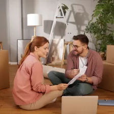 Jeune couple assis par terre, déballant des boîtes et planifiant leur aménagement.