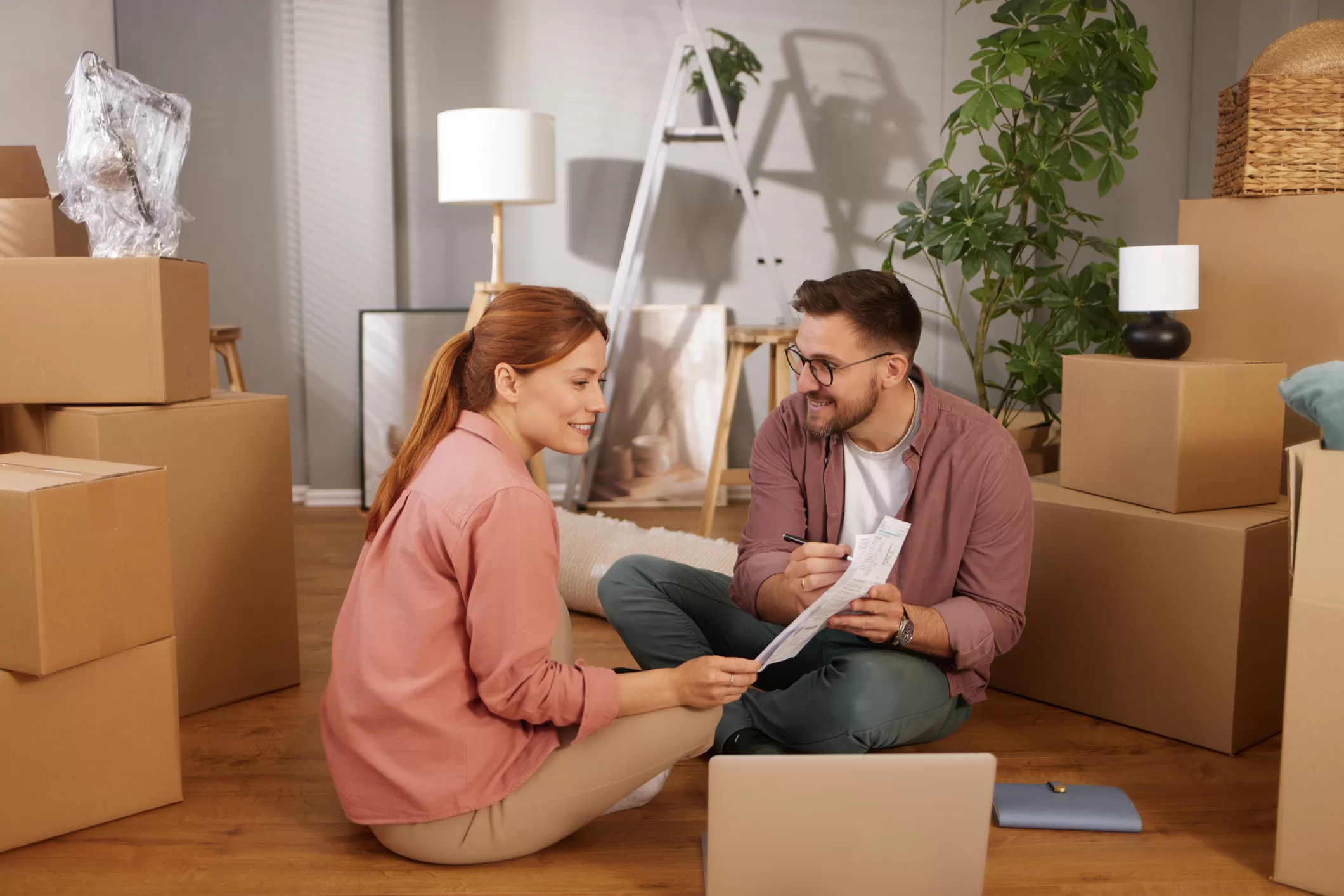 Jeune couple assis par terre, déballant des boîtes et planifiant leur aménagement.