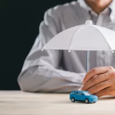 une main tenant un parapluie blanc au-dessus d'une petite voiture bleue