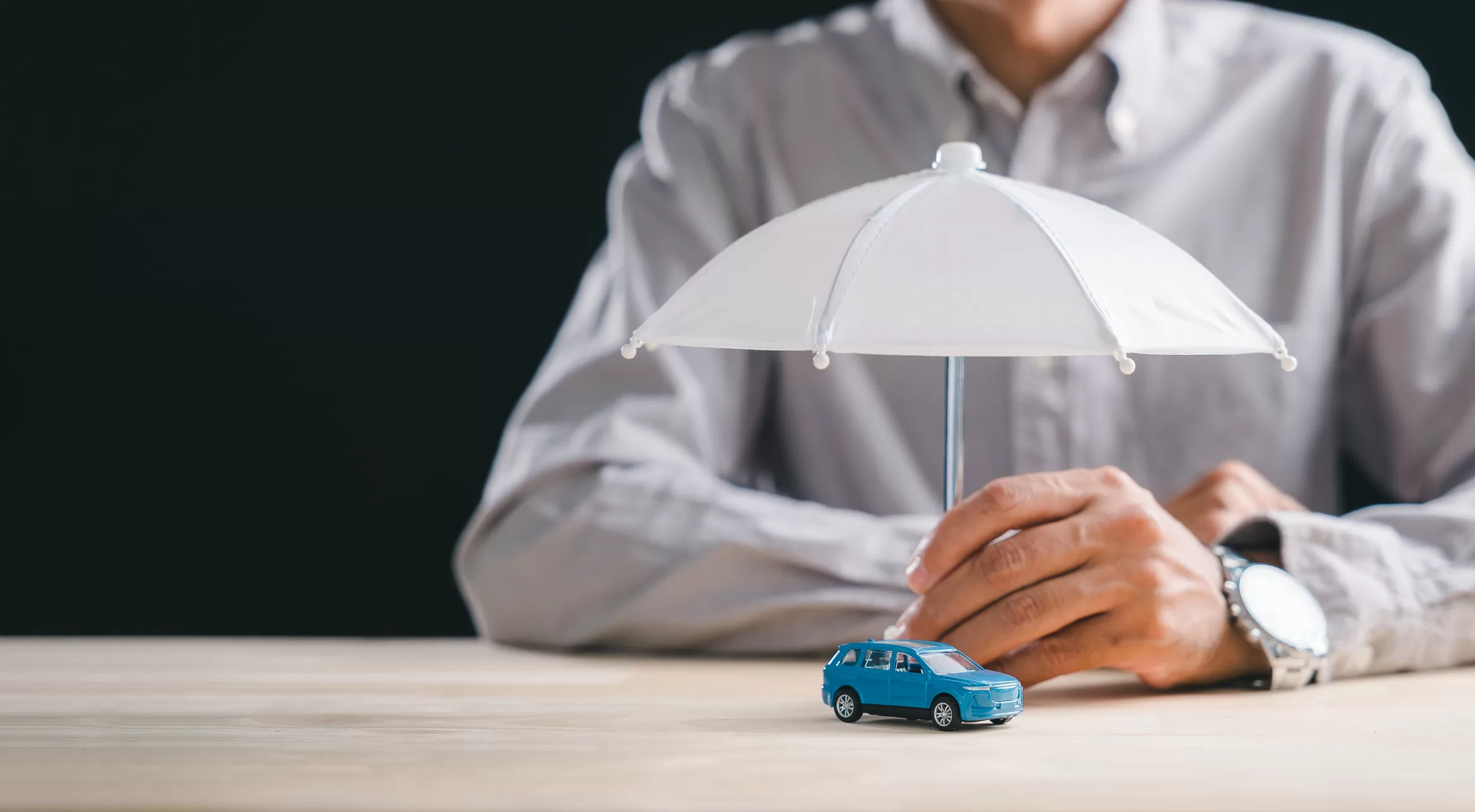 une main tenant un parapluie blanc au-dessus d'une petite voiture bleue