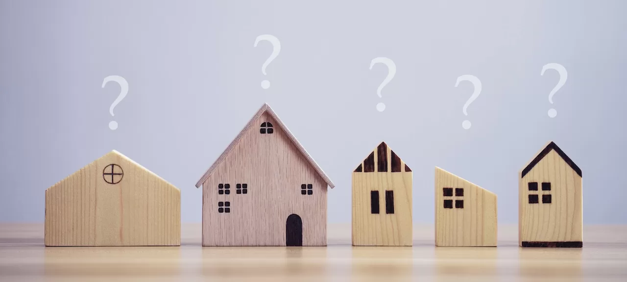 A row of small wooden houses arranged on a table, topped with question marks